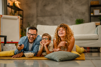 Family -father, mother and son enjoying at home sitting on the floor eating popcorns while watching TV